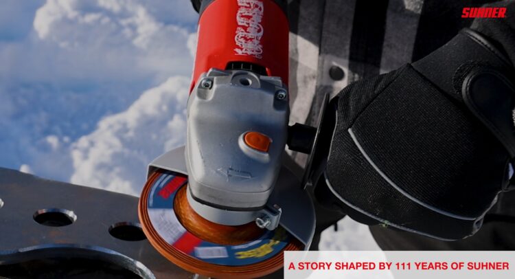 Close-up of a red and gray angle grinder with an orange grinding wheel mounted on a metal surface, outdoors; Sunner branding visible in the corner.